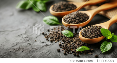 Dry black tea in wooden spoons and green leaves on black background with copy space. Dry black tea in wooden spoons and green leaves on black background with copy space. 124450005