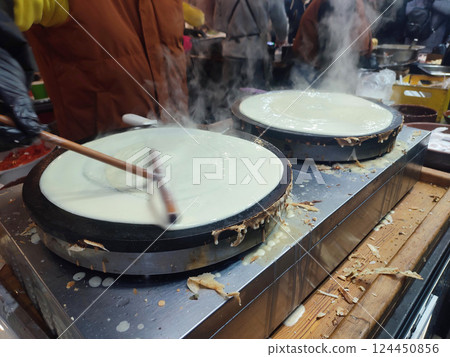 Frying pancakes. Person chef spreading liquid batter on round frying pan spatula. Cooking food on street. Festivities festival. Street food fried batter dough. Frying pancakes. Person chef spreading liquid batter on round frying pan spatula. Cooking food on street. Festivities festival. Street food fried batter dough. 124450856
