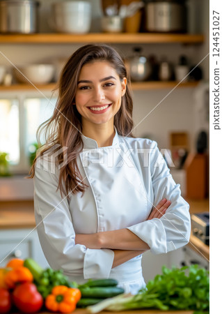 A woman in a chef's uniform standing in a kitchen with her arms crossed 124451027