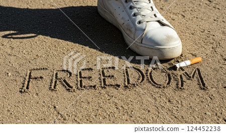 Foot stomping on a cigarette with Freedom written in the sand, symbolizing quitting smoking and gaining freedom from addiction. 124452238