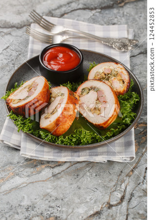 Baked Turkey breast roll with bacon, onions and mushrooms served with tomato sauce close-up in a plate. Vertical 124452853
