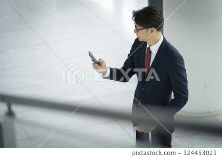 一位 40 多歲的商人背著手提包，看著智慧型手機螢幕 124453021