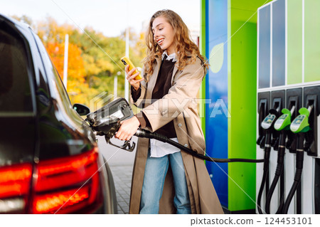Young woman filling her car at the gas station. You can Online pay. Woman pays for a gas station 124453101