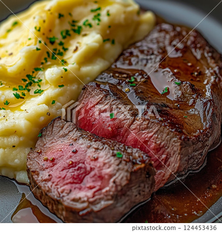 Juicy sliced ribeye steak resting on a bed of creamy mashed potatoes, drizzled with garlic butter sauce and garnished with fresh parsley Juicy sliced ribeye steak resting on a bed of creamy mashed potatoes, drizzled with garlic butter sauce and garnished with fresh parsley 124453436