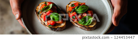 Chef holding plate with two slices of toasted bread topped with fresh tomatoes, basil, and seasonings, creating a classic italian bruschetta appetizer 124453447