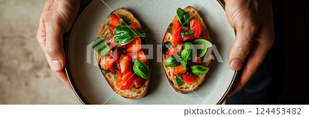 Chef holding plate with two slices of toasted bread topped with fresh tomatoes, basil, and seasonings, creating a classic italian bruschetta appetizer Chef holding plate with two slices of toasted bread topped with fresh tomatoes, basil, and seasonings, creating a classic italian bruschetta appetizer 124453482