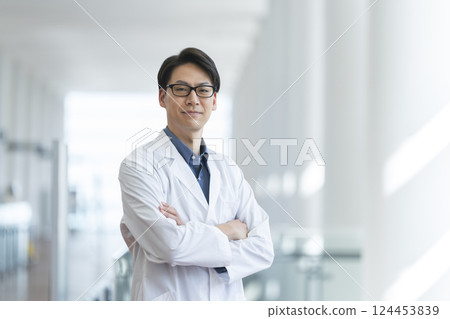 A man in his 40s wearing a white coat with his arms crossed, smiling at the camera 124453839