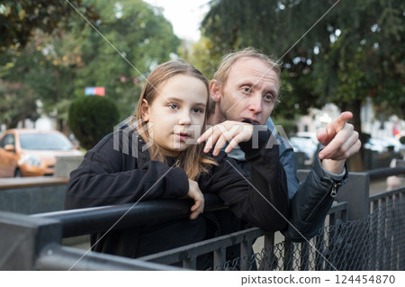 Cheerful daughter child girl and her father together looking at something and pointing. Cheerful daughter child girl and her father together looking at something and pointing. 124454870