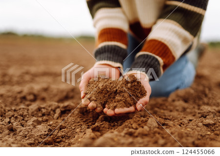 Young female farmer's hands touch dry soil in an agricultural field. Gardening and ecology concept. Young female farmer's hands touch dry soil in an agricultural field. Gardening and ecology concept. 124455066