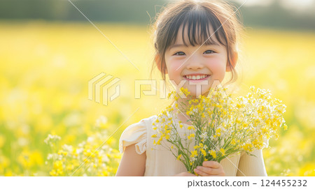 A girl holding a bouquet of rapeseed flowers and gazing at them with a smile 124455232