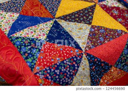 Bright, colorful patchwork quilt featuring variety of floral patterns and symmetrical designs. Mottled background 124456690