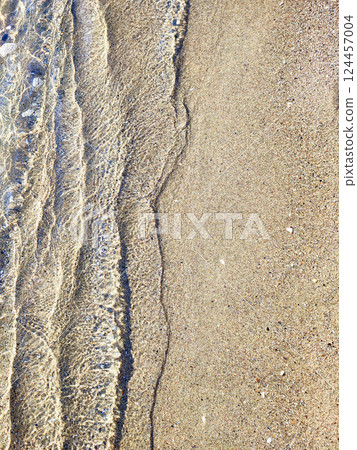 Abstract view of waves of clean transparent water of the sea on the sand of the beach of the seashore on a sunny day. Waves with shadows rolling onto a sandy beach close-up. Sun glare on sandy bottom 124457004