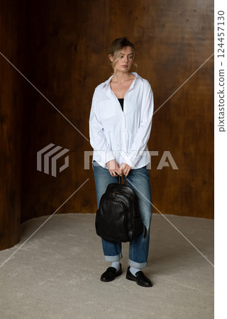 A girl in a white shirt blue jeans and loafers is posing with a backpack. A girl in a white shirt blue jeans and loafers is posing with a backpack. 124457130