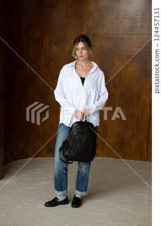 A girl in a white shirt blue jeans and loafers is posing with a backpack. A girl in a white shirt blue jeans and loafers is posing with a backpack. 124457131