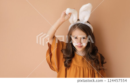 A cute girl in the guise of an Easter bunny adjusts the ear of her headdress. Easter Day Banner A cute girl in the guise of an Easter bunny adjusts the ear of her headdress. Easter Day Banner 124457554
