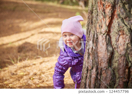 A child looks out from behind a tree on an autumn day. A child looks out from behind a tree on an autumn day. 124457796