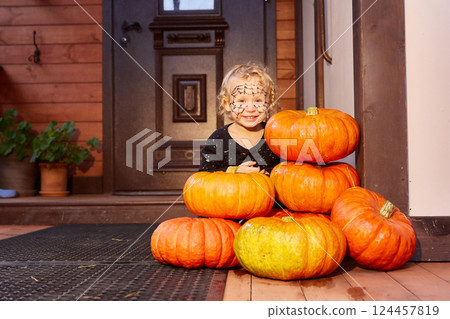 a child celebrates Halloween. The porch and front door of the house are decorated with pumpkins. Halloween decor 124457819