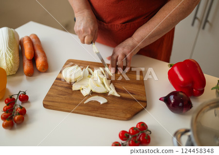 Woman cutting red onion into rings at wooden table, closeup 124458348