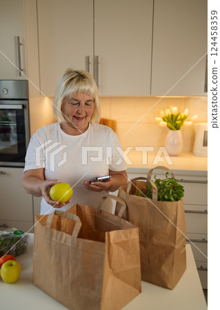 Senior woman unpacking groceries from paper bags in the kitchen Senior woman unpacking groceries from paper bags in the kitchen 124458359