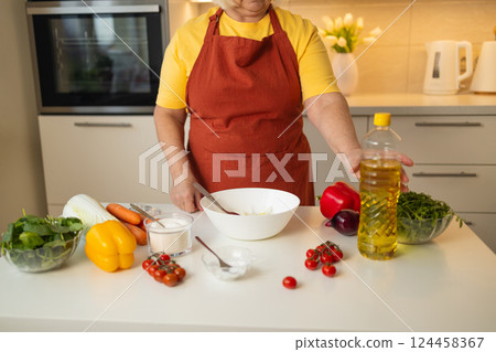 Senior Woman Pouring Oil into a Bowl for Cooking in a Modern Kitchen 124458367