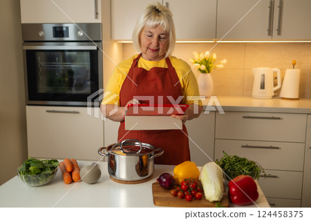 Senior woman in the kitchen using a tablet while preparing ingredients. 124458375