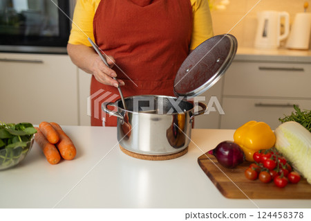 Cooking vegetables in a pot, stirring the ingredients with a spoon Cooking vegetables in a pot, stirring the ingredients with a spoon 124458378