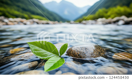 fresh green leaf rests smooth stone clear mountain stream, surrounded by serene natural environment with blurred forested hills background 124458430