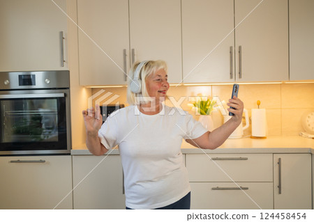 Senior woman listening to music in the kitchen, enjoying the moment Senior woman listening to music in the kitchen, enjoying the moment 124458454