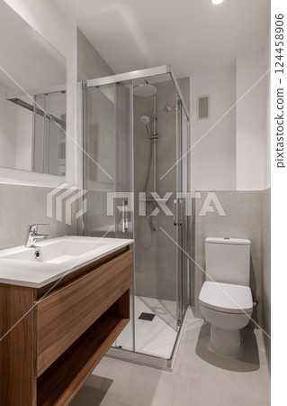 Modern bathroom with a glass-enclosed shower, wooden vanity, and neutral tiles 124458906