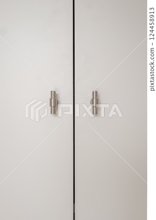 Minimalist white wardrobe doors with modern stainless steel handles in symmetrical alignment 124458913