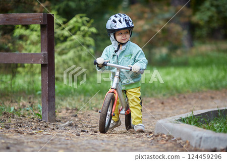 Child on a running balance bike on an autumn or summer cold day. Mittens on the hands Child on a running balance bike on an autumn or summer cold day. Mittens on the hands 124459296