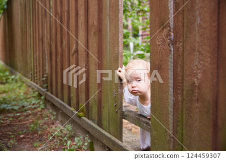 bored child looks through a hole in a brown fence. Summer day. bored child looks through a hole in a brown fence. Summer day. 124459307