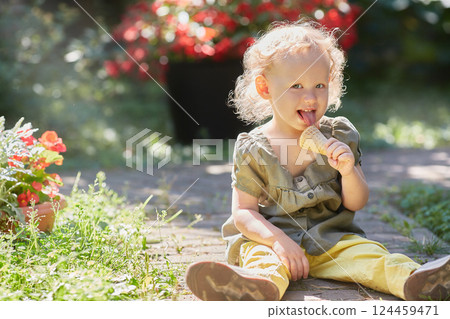 Happy toddler with ice cream is sitting on the grass in in the rays of the sun. 124459471