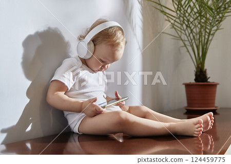 small child uses a mobile phone with headphones on his head. small child uses a mobile phone with headphones on his head. 124459775
