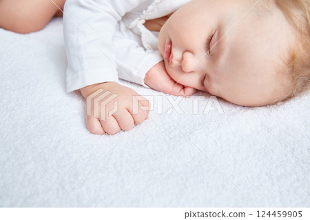 Cute baby sweetly sleeps on white bed linen in white clothes. Close-up. Beautiful healthy soft skin, long eyelashes. 124459905
