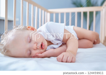 Baby sleeps in baby wooden crib for newborns. A spacious, bright room with a date palm tree in the background. 124459911