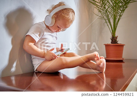 small child uses a mobile phone with headphones on his head. 124459921