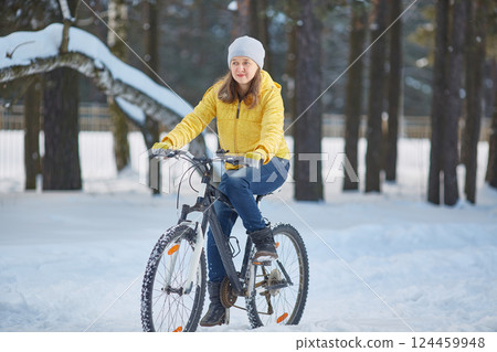 Woman in a bright yellow jacket rides a bicycle in winter in the snow 124459948