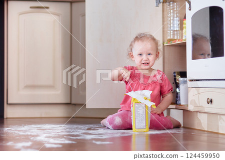 A child sits in a dirty heap of flour scattered on the floor in the kitchen at home. Copy space 124459950
