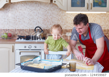 Dad teaches the small child to preparing baking cookies or pastries together. Family leisure at home in the kitchen. 124459987