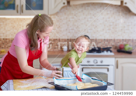 Mom and her toddler bake pies in the kitchen at home. The child greases cheesecakes with a cooking brush. Lifestyle. 124459990
