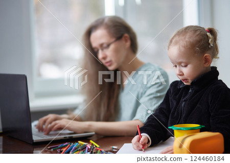A girl draws with pencils while working as a freelancer's mother. The concept of working at home and taking care of the family A girl draws with pencils while working as a freelancer's mother. The concept of working at home and taking care of the family 124460184