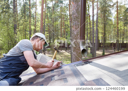 The master attaches a soft tile roof to the roof of a country house. 124460199
