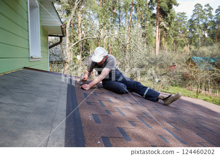 A man repairs a roof made of flexible tiles on a sunny summer day in a pine forest. 124460202