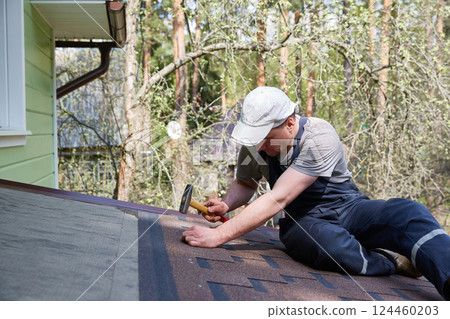 A worker installs a soft roof on the roof of a country house. Made of modified bitumen and stone chips based on fiberglass. 124460203