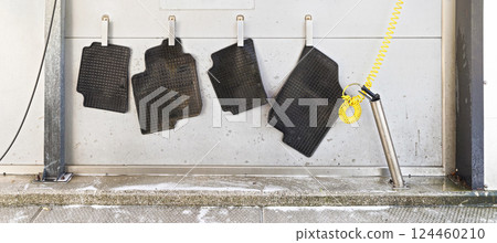 Black rubber car mats hanging on steel pegs to dry in carwash after being washed 124460210