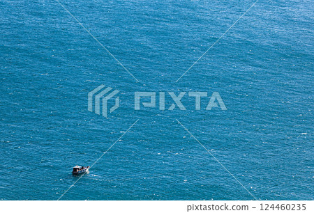 Solitary boat in the vast expanse of the deep blue sea, aerial view. Perfect for travel themes, tranquility concepts, or marine-themed designs. Solitary boat in the vast expanse of the deep blue sea, aerial view. Perfect for travel themes, tranquility concepts, or marine-themed designs. 124460235
