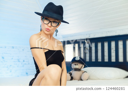 Sexy girl with glasses and a hat in the image of a gangster, with short hair posing at home in the bedroom against the background of a teddy bear in a police cap and handcuffs 124460281