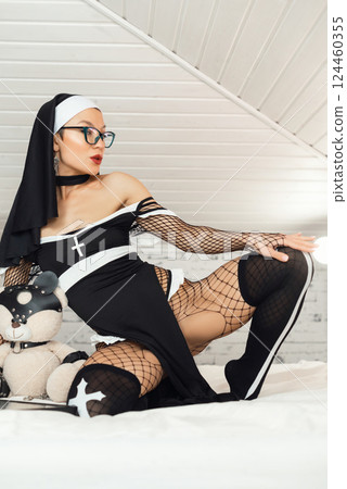 A girl in a sexy nun dress from an adult role-playing sex shop and stockings excitingly poses on a bedroom bed 124460355