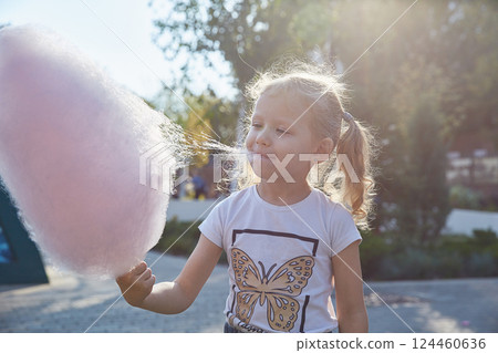 Curly-haired girl enthusiastically eats cotton candy. The concept of a family of children and happiness with children. Curly-haired girl enthusiastically eats cotton candy. The concept of a family of children and happiness with children. 124460636